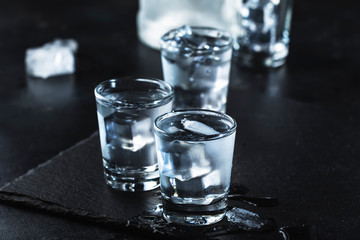 Vodka in shot glasses on black stone background, iced strong drink in misted glass