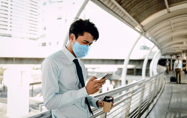 Naklejka na ściany i meble Young Asian Businessman Wearing a Surgical Mask and Using a Smart Phone in City. Healthcare in New Normal Lifestyle Concept