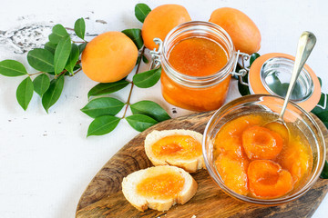 Homemade apricot jam in glass bowl and in jar, prepared for eating. Sandwiches with fresh homemade apricot jam on the cutting board. Healthy fruit eating.
