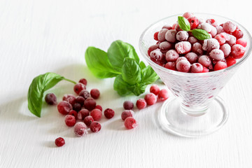 Frozen cranberries in glass vase and on the white table. Healthy frozen fruits.