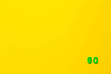 A green plastic toy number eighty is located in the lower right corner on a yellow background