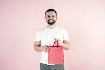 A young and handsome man with a beard and a gift bag. Pink background.