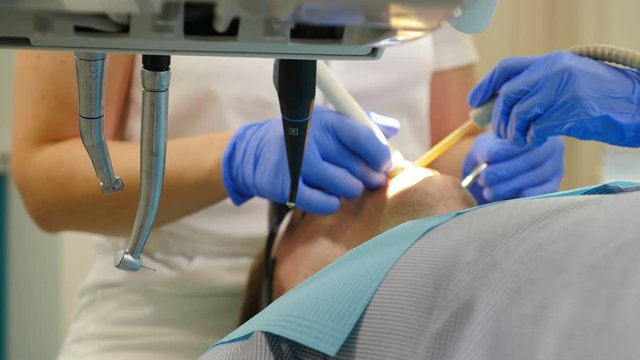 Dental curing shot through dental tools. Close-up of treatment in modern dentistry. side view. Dentist at work. Male patient Undergoes Medical surgical intervention and Oral Cavity Treatment. 4 k