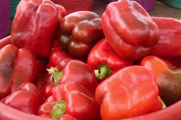 A basket of red peppers in a red basket set up at a farmer's market