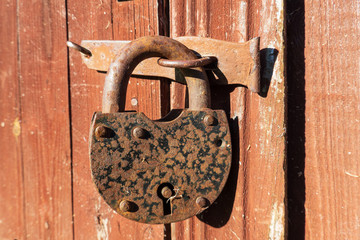 Old rusty padlock closes the door of a brown wooden house. Close-up. Background. Texture.