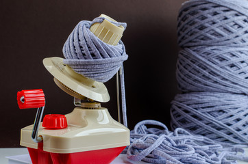 hand plastic wool winder at work, gray yarn balls, brown background. prepair for knitting, crochet....