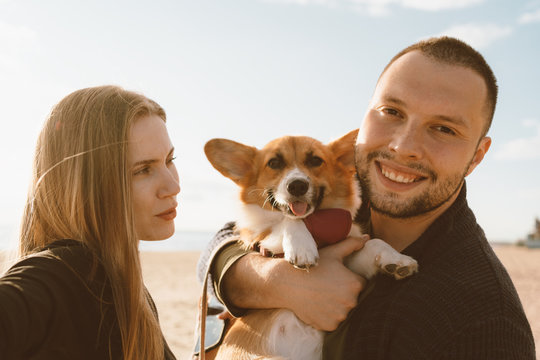 Young happy couple with dog taking selfie on beach. Beautiful woman and man and Corgi puppy are having fun. Family life, togetherness, husband and wife relax together in summer by sea - Powered by Adobe