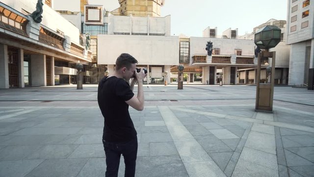 Young man photographs popular buildings in city. Action. Guy takes professional photos of modern urban architecture. Photographer takes pictures of large city building
