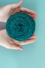 closeup female hands holding ball of teal wool yarn ball on teal background