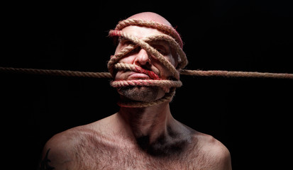 Image of binded bald adult man with rope on face