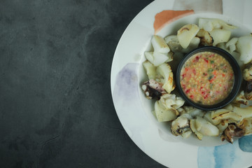 Grill squid served with a spicy sauce in dish on a black background