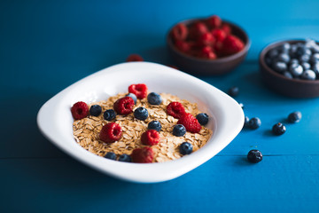 Studio view of oat with blueberry and raspberry over blue wooden backdrop.