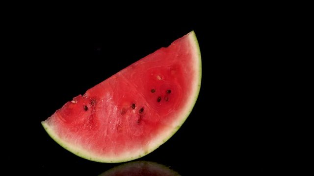 Slow motion showing swinging slice of fresh pink watermelon with black background