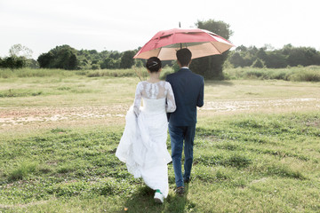 The bride and groom walked to an umbrella on the meadow.