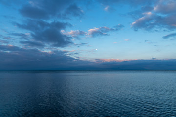 Beautiful sunrise on the lake with full moon and dramatic blue clouds .