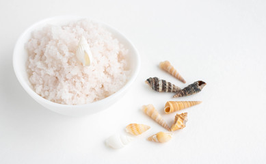 White bowl with pink salt and shells on a white background