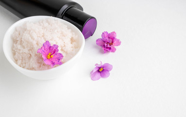 Fototapeta na wymiar An oval white bowl with pink salt stands on a white background next to it are a black bottle and violet flowers