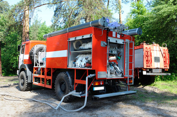Fire engine parked in a forest, hoses connected, fire-fighting equipment prepared for use