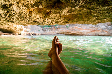 POV shot of the legs of a person chilling inside a beach cave in Mallorca, at the Mediterranean Sea