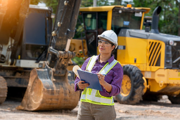 Female engineer worker on construction site outdoors with excavator in background,construction...