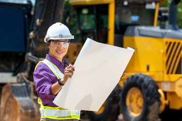 Female engineer worker on construction site outdoors with excavator in background,construction...
