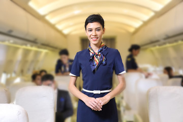 Caucasian flight attendant posing with smile at middle of the aisle inside aircraft with passengers...