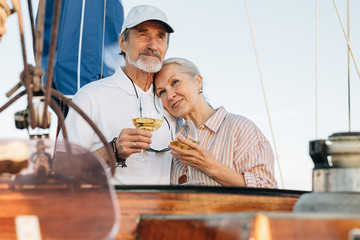Mature couple standing on a private yacht and drinking wine. Two senior people enjoy sailing and...