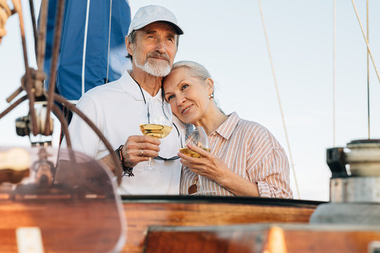 Mature couple standing on a private yacht and drinking wine. Two senior people enjoy sailing and each other.