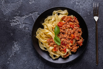 Traditional italian pasta bolognese on a black plate.