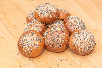 stack of small brown breads with white and black sesame on wooden table, used for burgers