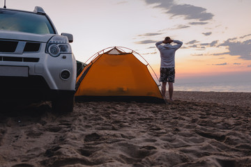 man standing near camping tent with suv car looking at sunrise