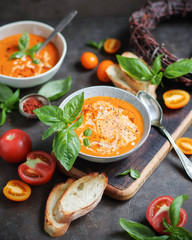 Tomato soup with basil in two ceramic bowls. Lots of tomatoes on the table. Vegetarian food. Red and yellow.