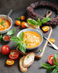Tomato soup with basil in two ceramic bowls. Lots of tomatoes on the table. Vegetarian food. Red and yellow.