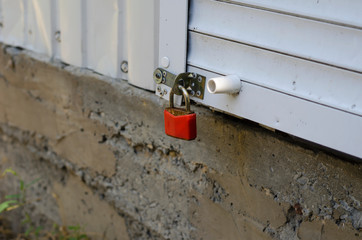 Close-up of a red padlock on the closed roller shutter of the store.