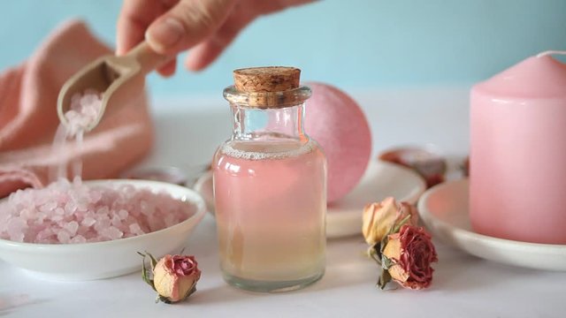 Pink bath salt and body care products with pink roses. Beauty treatment. Spa relax concept. Woman hand stirring salt with wooden spoon