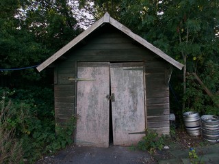 Discarded old wooden shed with silver barrels to the side