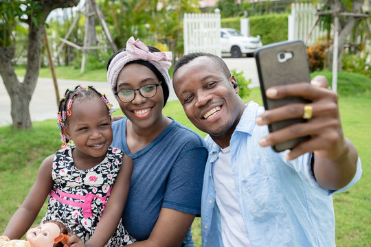 A warm family of black Americans is taking pictures of the family with a smartphone.  They have a bright and friendly smile.  Concepts of relationship building and leisure activities in the garden.