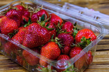 Plastic container with pile of ripe strawberries on wooden table