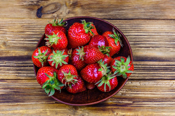 Ceramic plate with pile of ripe strawberries on wooden table