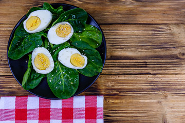 Spinach leaves and halved boiled eggs on a black plate. Top view