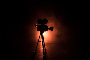 Movie concept. Miniature movie set on dark toned background with fog and empty space. Silhouette of vintage camera on tripod.