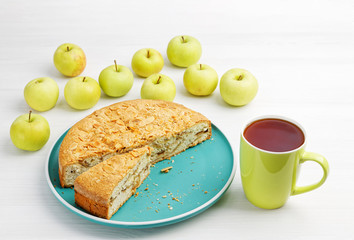 Homemade pastry. Apple pie with almond petals and cup of tea on white wooden table.