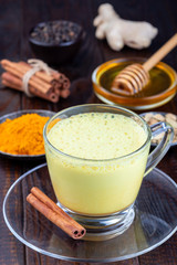 Moon milk with turmeric in glass cup, ingredients on background, vertical