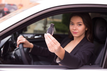 Fototapeta na wymiar Just take your key from your new car. Side view of beautiful young woman looking at camera and holding a car key while sitting in car