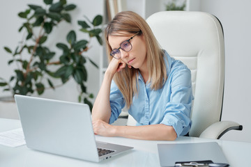 Young tired businesswoman with blond hair looking unhappily at laptop display