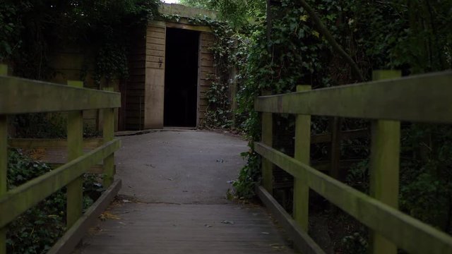 Walking over small wooden bridge leading to a doorway medium shot
