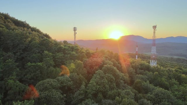 Rising aerial over dense green mountains with 5G telecommunication towers standing tall on them during golden hour