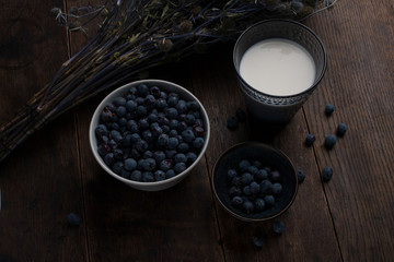 Glass of milk, cup and bowl of blueberries and thistle branch on the old wooden table