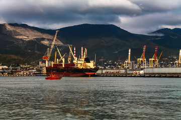 The seaport on the background of mountains during cloudy, cloudy weather in the mountains. Moored for unloading / loading sea ships against the background of mountains in the clouds.