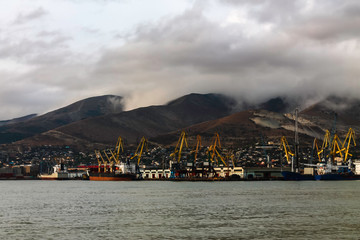 The seaport on the background of mountains during cloudy, cloudy weather in the mountains. Moored for unloading / loading sea ships against the background of mountains in the clouds.